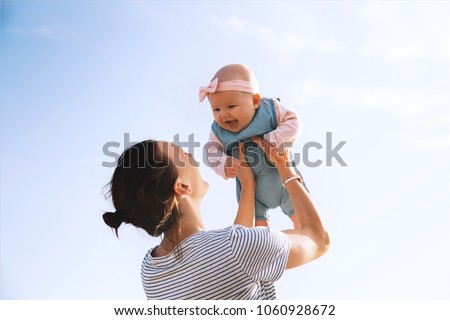 Young mother throws up baby in the sky, summer outdoors. Happy mom and cute smiling baby girl. Positive human emotions, feelings, natural lifestyles. Family background.