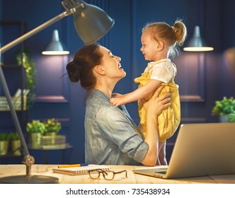 Young Mother With Toddler Child Working On The Computer From Home At Night. 