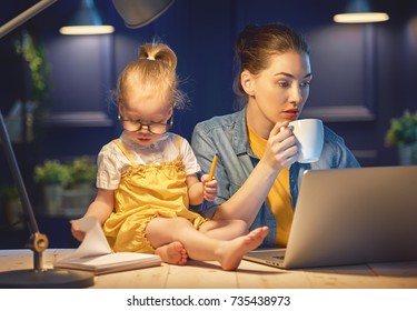 Young mother with toddler child working on the computer from home at night. 