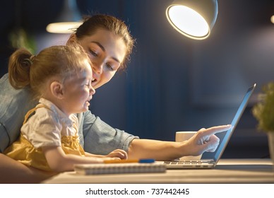 Young Mother With Toddler Child Working On The Computer From Home At Night. 