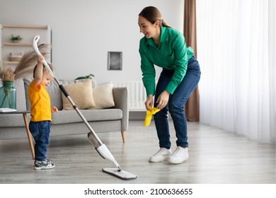 Young Mother And Toddler Son Cleaning At Home Together, Mom Teaching Kid Chore Help Home Work. Little Boy Holding Mop, Cleaning Floor In Living Room