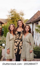 A Young Mother, Together With Two Twin Daughters In Beautiful Dresses, Are Standing And Smiling. Family Portrait. Twins In Braces.