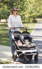 Young Mother With Twin Babies In Stroller Walking Outdoors