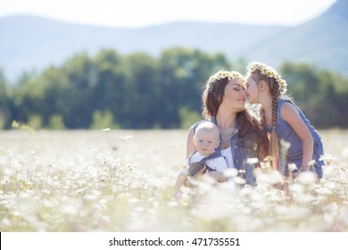 Young Mother With Two Children In Chamomile Field. Mother And Two Children Having Fun In Field Outdoors. Happy Family On Summer Day. Mum With Baby And Kid.