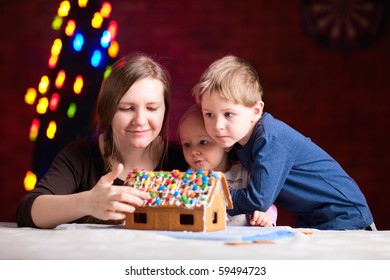 Young Mother And Two Kids Making Gingerbread House On Christmas Eve