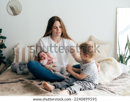 A young mother with two small children spends time in the bedroom at home.