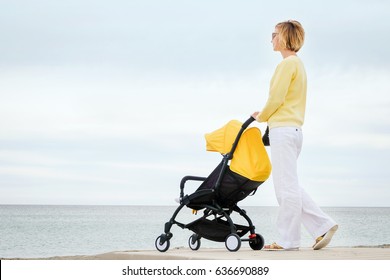 Young mother walking at the beach with baby stroller against cloudy sky - Powered by Shutterstock