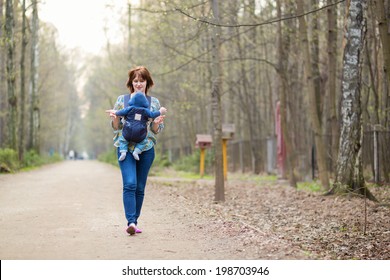 Young Mother Walking In Forest With Her Baby In Carrier