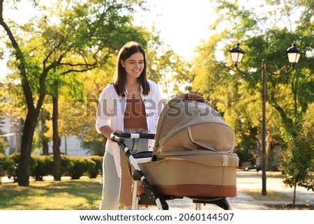 Young mother walking with her baby in stroller at park on sunny day