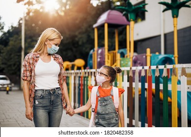 Junge Mutter geht mit ihrer kleinen Tochter auf der Stadtstraße spazieren. Sie tragen Gesichtsschutzmasken. Zurück zur Schule und das neue Coronavirus-Lifestyle-Konzept.