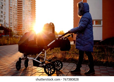 Young Mother Walking In A Park With Children In Pushchair. Mom And Kids In A Buggy Walk In Forest. Woman Pushing A Double Stroller For Twin Boy Newborn Baby. Active Family Outdoors.