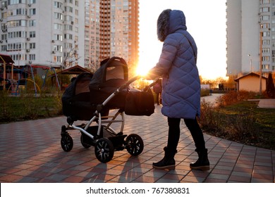 Young Mother Walking In A Park With Children In Pushchair. Mom And Kids In A Buggy Walk In Forest. Woman Pushing A Double Stroller For Twin Boy Newborn Baby. Active Family Outdoors.