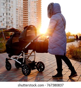 Young Mother Walking In A Park With Children In Pushchair. Mom And Kids In A Buggy Walk In Forest. Woman Pushing A Double Stroller For Twin Boy Newborn Baby. Active Family Outdoors.