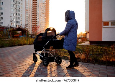 Young Mother Walking In A Park With Children In Pushchair. Mom And Kids In A Buggy Walk In Forest. Woman Pushing A Double Stroller For Twin Boy Newborn Baby. Active Family Outdoors.