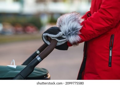 young mother walking with stroller in winter with protection on handles against winter