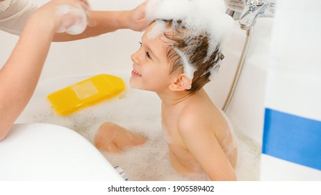 young mother washing off shampoo from her little son under shower in bathroom. Concept of child hygiene and health care at home. Family having time together and playing at home.