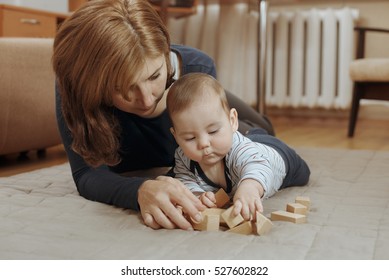 Young Mother Watching Over Her Cute Little Baby Boy As He Plays On The Carpet In The Living Room With Wooden Blocks In A Close Up Low Angle Portrait