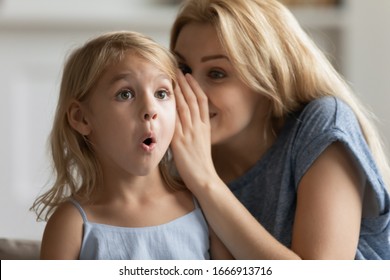 Young mother whisper in surprised cute little daughter ear tell secret, millennial mom or nanny play with small preschooler girl child, share close intimate moment at home, gossip or chat together - Shutterstock ID 1666913716