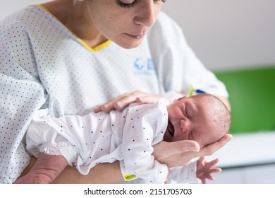 young mother who has just had her baby in the hospital holds the newborn in her arms gently patting him on the back to help him pass gas after feeding