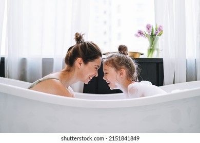 Young mother woman with long hair with little tween girl daughter in pajamas having fun in the bath with foam at home - Shutterstock ID 2151841849
