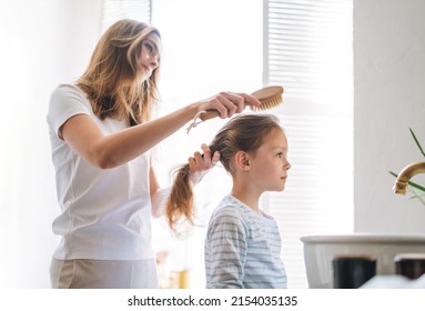 Young Mother Woman With Long Hair With Little Tween Girl Daughter In Pajamas Combs Her Hair On Morning In Bathroom At Home