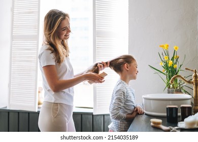 Young Mother Woman With Long Hair With Little Tween Girl Daughter In Pajamas Combs Her Hair On Morning In Bathroom At Home