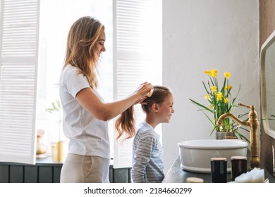 Young Mother Woman With Long Hair With Little Tween Girl Daughter In Pajamas Combs Her Hair On Morning In Bathroom At Home