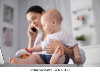 Young mother working in a decree at the computer with a baby son in her arms