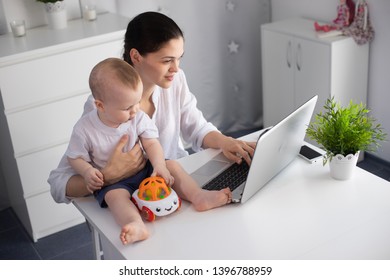 Young mother working in a decree at the computer with a baby son in her arms - Shutterstock ID 1396788959