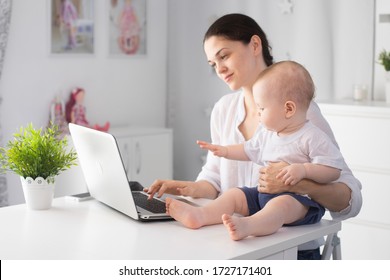 Young mother working in a decree at the computer with a baby son in her arms - Shutterstock ID 1727171401