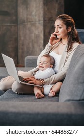 Young mother working from home, talking on smartphone while spending time with her baby boy