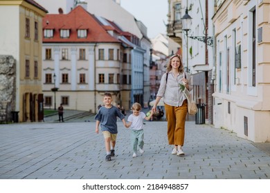 Young mother with zero waste shopping bag holding hands with her children and walking in old city street center. - Powered by Shutterstock