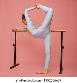 Young motivated determined woman in sportswear  leggings stretching legs on ballet barre standing on pink background focused exercising, preparing muscles working-out
 - Powered by Shutterstock