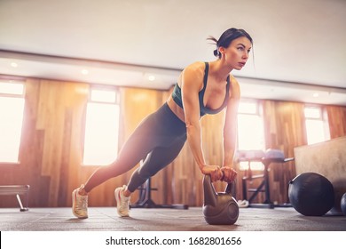 young motivated girl doing plank exercise using kettlebells at gym, full length photo, copy space.