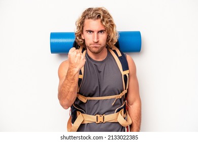 Young mountaineer caucasian man with a big backpack isolated on white background showing fist to camera, aggressive facial expression.