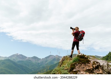 Young Mountaineer Woman With Backpack Taking Pictures On A Rock During A Mountain Hike.