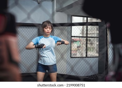 A Young Muay Thai Novice Holds Both Of Her Arms Up While Her Elbows Are Tucked To The Sides As She Prepares To Twist And Stretch Her Back And Arms Before Training.