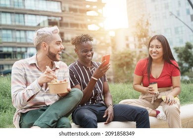 Young Multi Ethnic Colleagues Coworkers Enjoying Conversation While Eating Take-out Street Food In The City Park During Job Meal Break. Focus On African Man