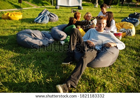 Young multi ethnic group of people watching movie at poof in open air cinema. Close up portrait of funny guy.