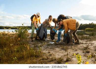 Young multi ethnic group of volunteers cleaning up the shore of a forest lake together, they are collecting trash and holding garbage bags. Concept of clean nature, ecology and sustainability. High - Powered by Shutterstock