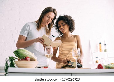 young multicultural couple looking at recipe in book at kitchen  - Powered by Shutterstock