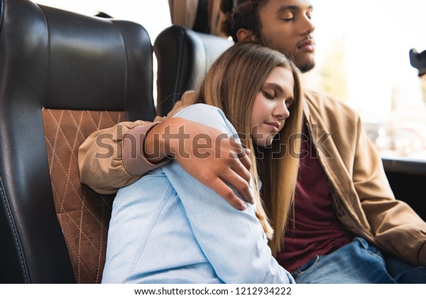 young multicultural couple of tourists sleeping\
during trip on travel bus