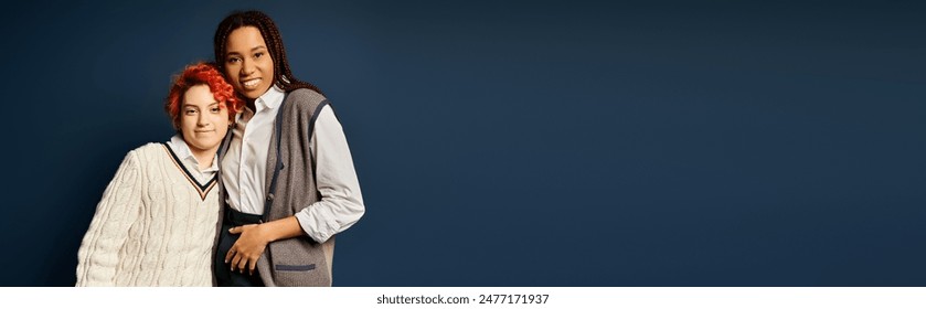 Young multicultural friends, including a nonbinary person, stand together in stylish attire against a dark blue wall.