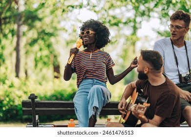 A young multicultural musicians having rehearsal in park on sunny summer day. Portrait of african american vocalist singing while guitar player playing a guitar in park. Musicians jamming in park. - Powered by Shutterstock