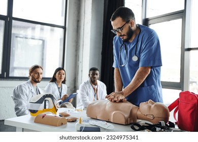 young multicultural students in white coats looking at medical instructor doing chest compressions on CPR manikin during first aid seminar, acquiring and practicing life-saving skills concept - Powered by Shutterstock