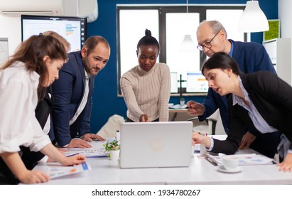 Young multicultural workers group talking, looking at laptop and analyzing digital datas Multiethnic colleagues working planning success financial strategy discussing in office