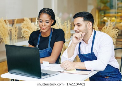 Young Multi-ethnic Cafe Owners Reading E-mails From Food Suppliers On Laptop Screen