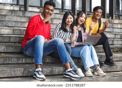 Young multiethnic college celebrating success while studying on laptop or working on group project while sitting on staircase or steps of college campus  - Shutterstock ID 2311788287