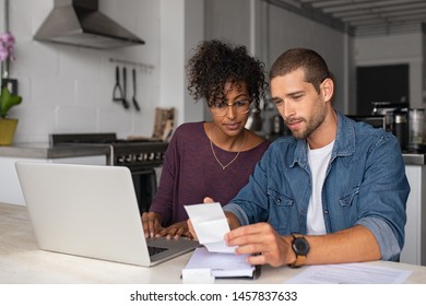 Young Multiethnic Couple Checking Bills While Managing Accounts On Home Banking App. Serious Casual Man And Girl Using Laptop While Looking At Invoice And Plan The Budget To Save.