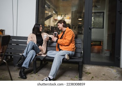 Young multiethnic couple with coffee to go talking on bench on cafe terrace - Shutterstock ID 2238308859